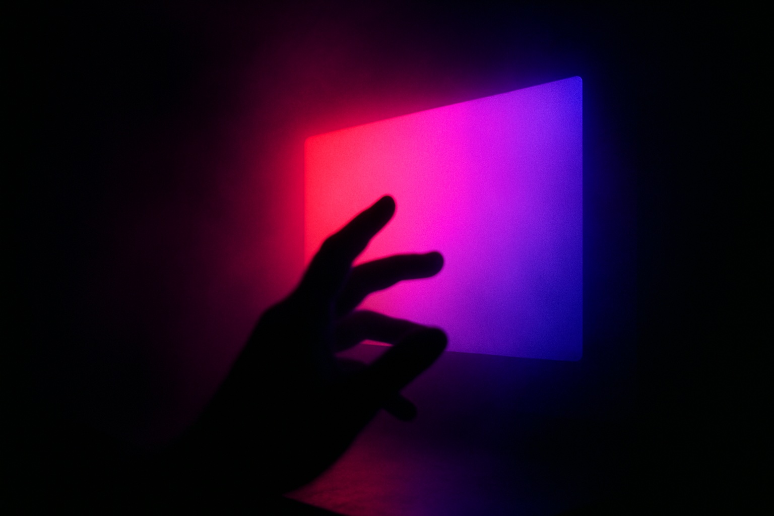 A cluttered desk in low light, stacks of books and a glowing monitor